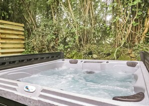 Un bain à remous doté d’un banc en bois et d’un logo, entouré d’une végétation luxuriante.