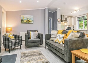 A modern living room with a grey sofa, two armchairs, a patterned rug, and a painting on the wall. - Deluxe lodge with one master double with an en suite shower and one twin. (Cartmel)