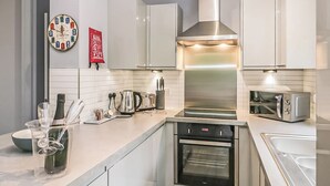 Une cuisine moderne dotée d’appareils électroménagers en acier inoxydable, de meubles blancs, d’un four encastré et d’une horloge murale.