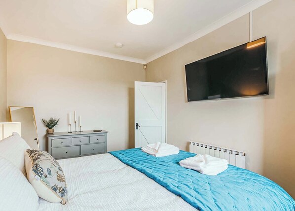 A bedroom with a bed, bedside table, lamp, TV, and a door.