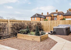 A backyard with a wooden fence, a hot tub, and a raised garden bed.