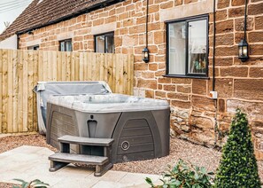 Una casa de piedra con jacuzzi, cerca de madera e iluminación exterior.