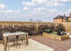 A patio with a table and chairs, a wooden fence, and a garden bed with plants. - A luxury three bedroom cottage perfect for families. (Bridgnorth)