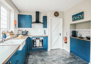 A modern kitchen with blue cabinets, a white door, a clock, and a fire extinguisher.