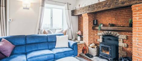 Een woonkamer met een blauwe bank, een open haard en een raam met gordijnen.
