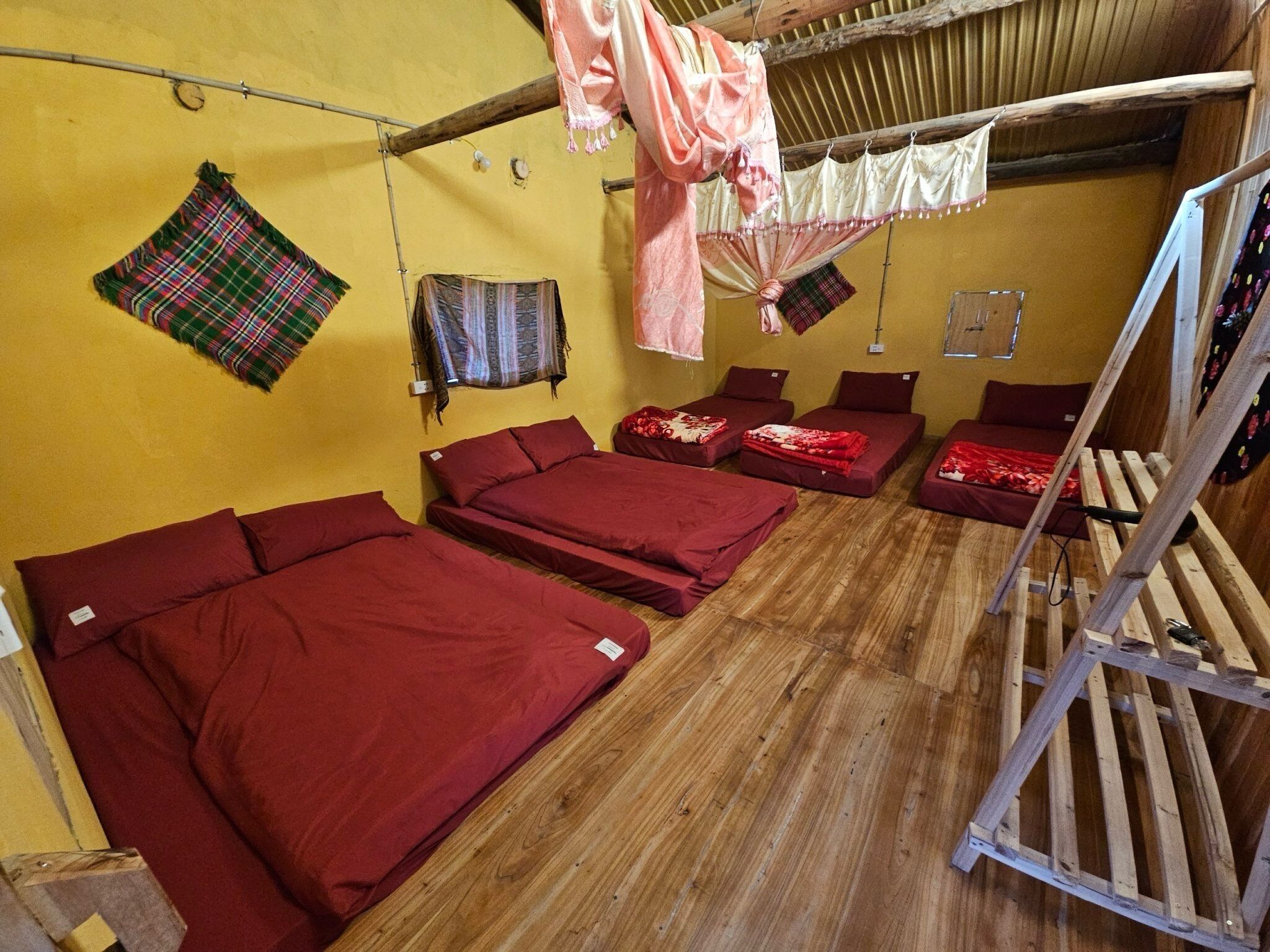 A dormitory room with four single beds, wooden flooring, and a bunk bed.