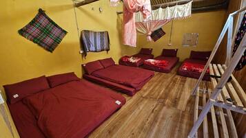 A dormitory room with four single beds, wooden flooring, and a bunk bed.
