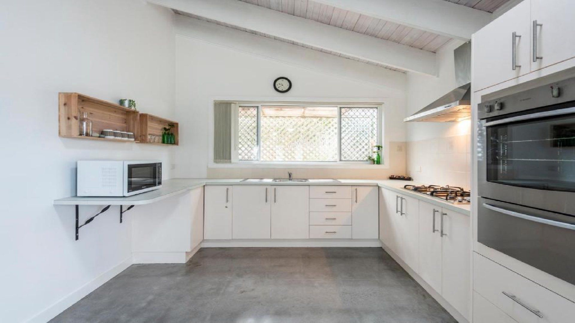 A modern kitchen with white cabinets, a microwave, a stove, and a window with a view.