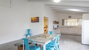 Zona pranzo con tavolo e sedie, cucina con frigorifero e finestra con decorazione a griglia.