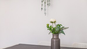 Una mesa de comedor con un jarrón de flores, una planta colgante y una silla blanca.