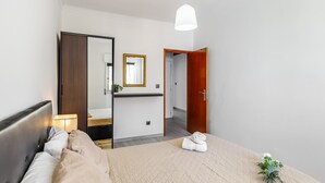 Una habitación de hotel con cama, espejo, puerta de madera, mesita de noche y lámpara colgante.