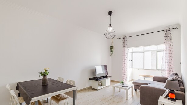 Una sala de estar moderna con una mesa de comedor, sofá, televisor y una planta colgante.