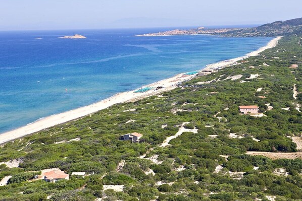 Paisaje costero con playa, abundante vegetación y algunos edificios.