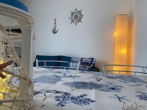 Una habitación con una cama, un adorno anclado a la pared, un timón de barco en la pared y una lámpara alta y vertical.