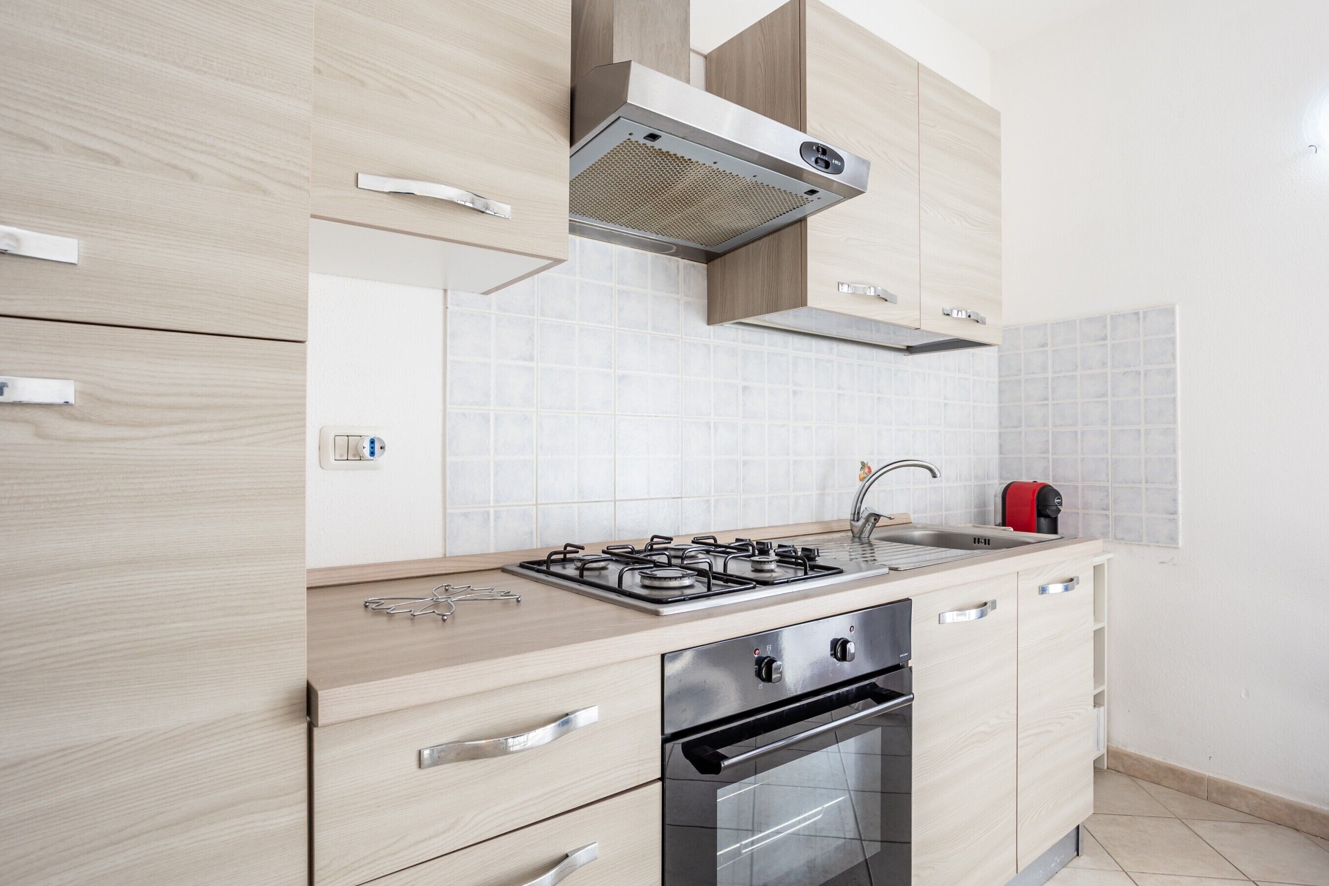 Eine moderne Küche mit hellen Holzschränken, einem Gasherd, einem Backofen und einer Edelstahl-Dunstabzugshaube.
