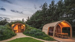 Une cabane en bois circulaire et accueillante, dotée d’une véranda et d’un coin repas séparé, le tout entouré d’une végétation luxuriante.