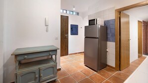 Eine Küche mit Kühlschrank, Holzschrank, blauer Tür und Fliesenboden.