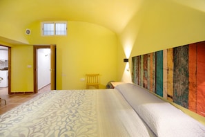 Une pièce comprenant un lit, une chaise en bois, une petite table, une lampe fixée au mur et une fenêtre.