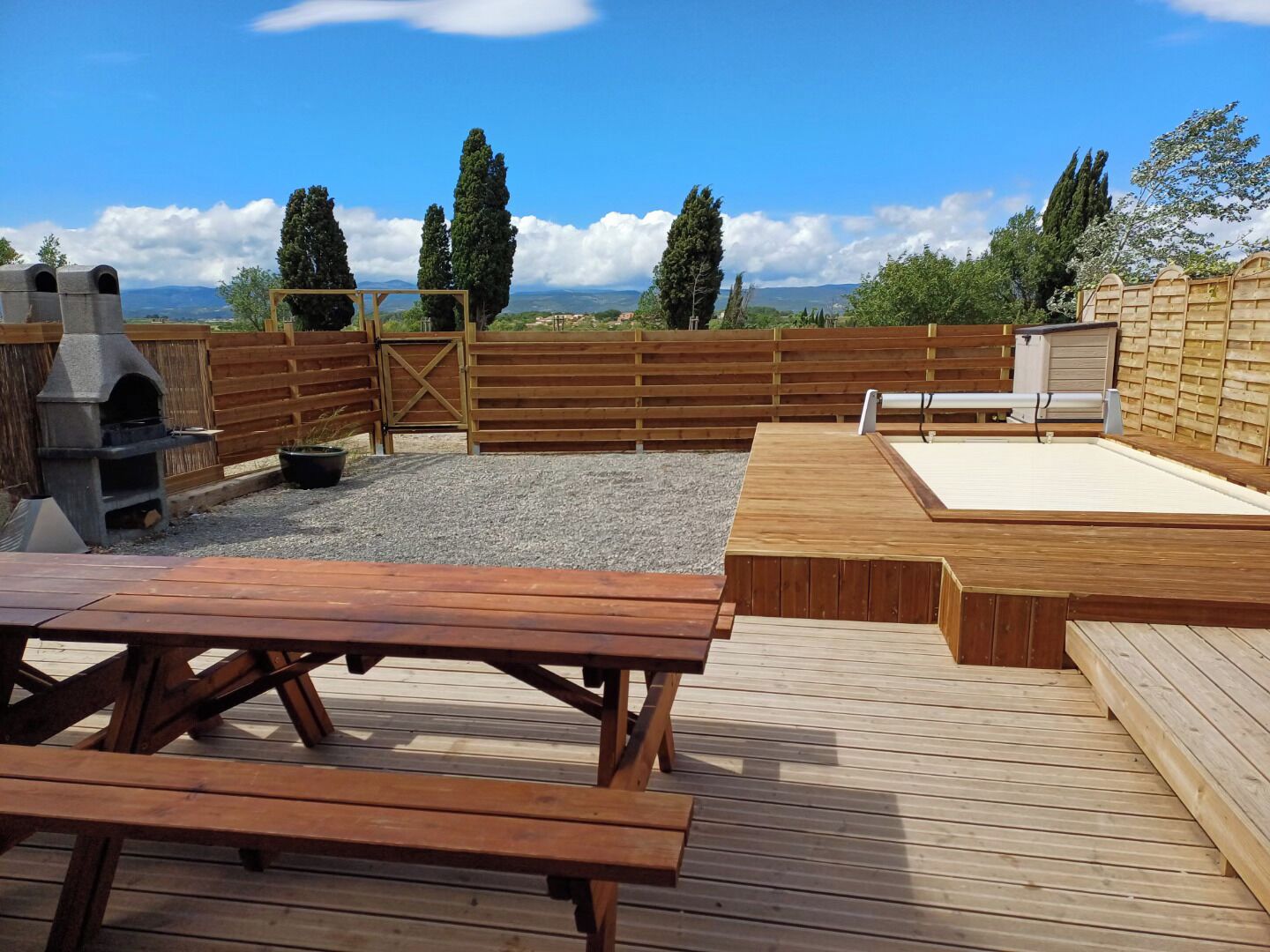 Une terrasse en bois avec des tables de pique-nique et un barbecue.