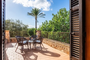 An open patio with wicker chairs and a table, a palm tree, and a stone wall.