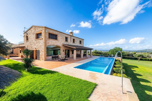 A two-story stone house with a swimming pool, outdoor seating, and a view of the countryside.