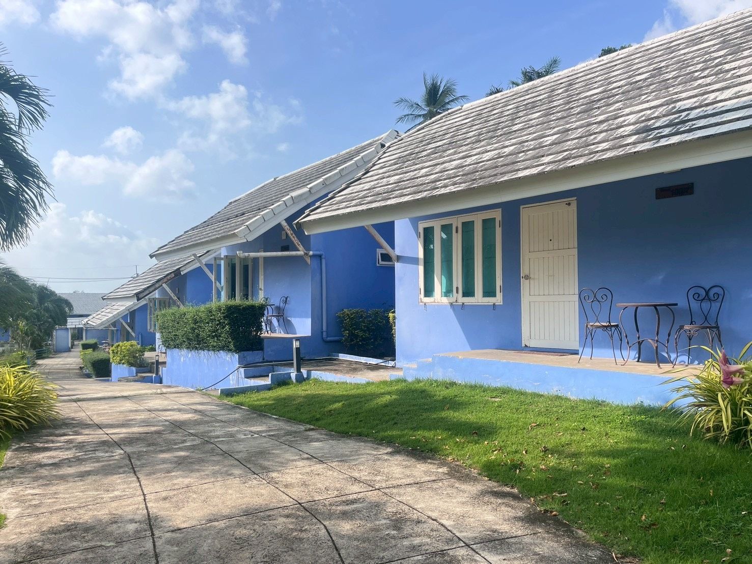 A row of blue buildings with a tiled roof, a paved pathway, and outdoor seating.