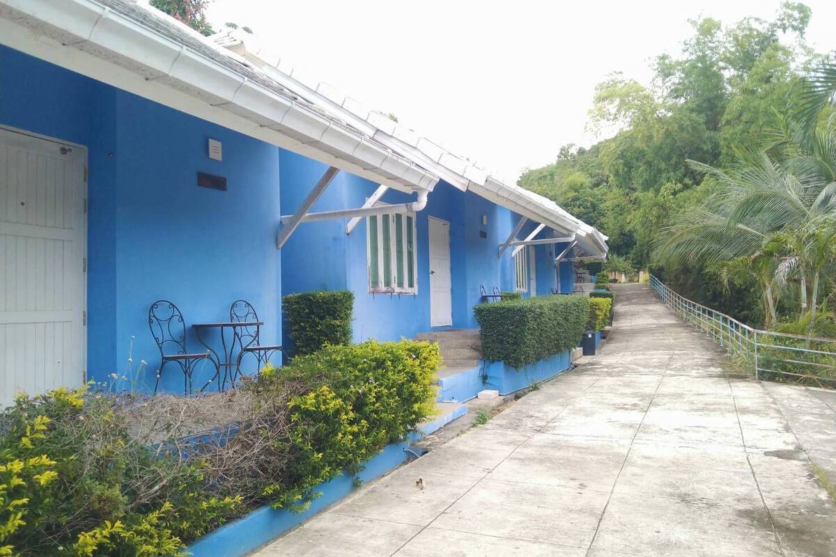 A blue building with a white door, a small porch with a table and chairs, and a concrete pathway leading to a staircase.