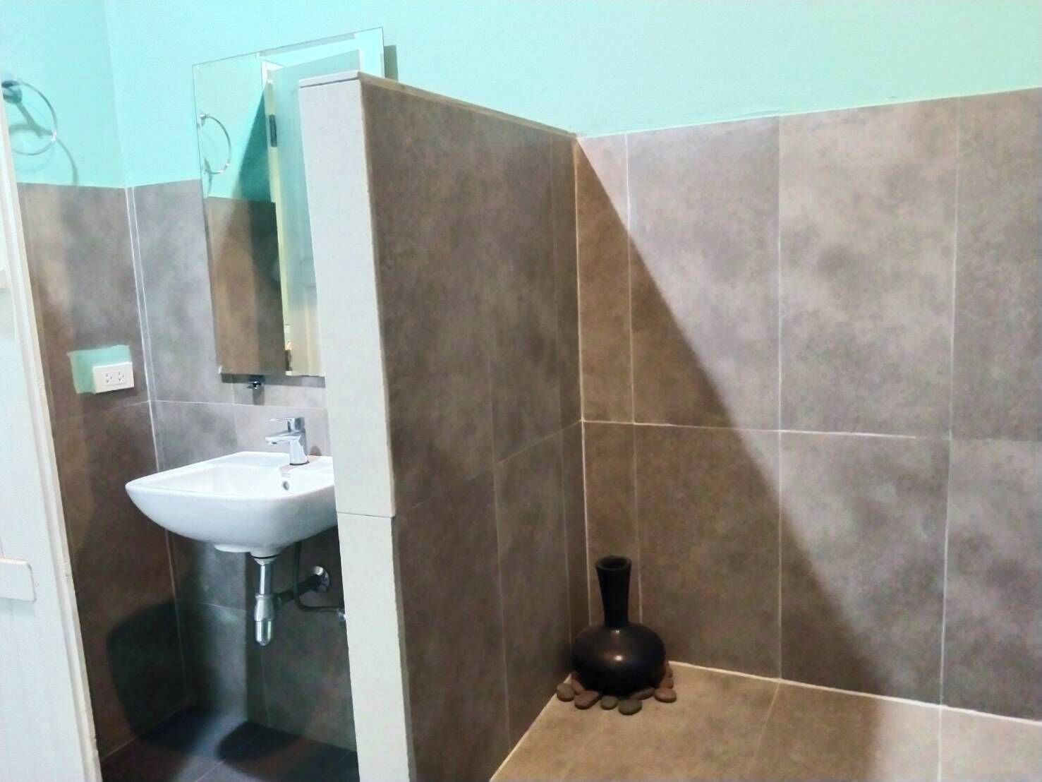Un baño con un lavamanos blanco, un espejo y un jarrón negro en el suelo.