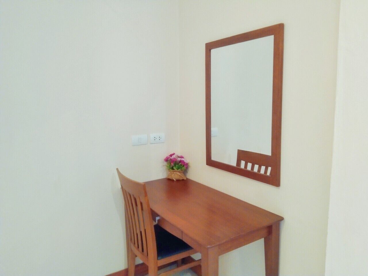 A small wooden desk with a chair, a mirror, and a vase with flowers.
