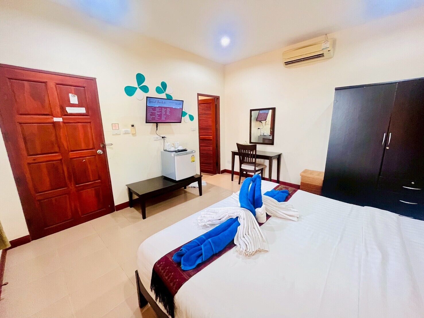 A hotel room with a bed, a desk, a chair, a wardrobe, and an air conditioning unit.