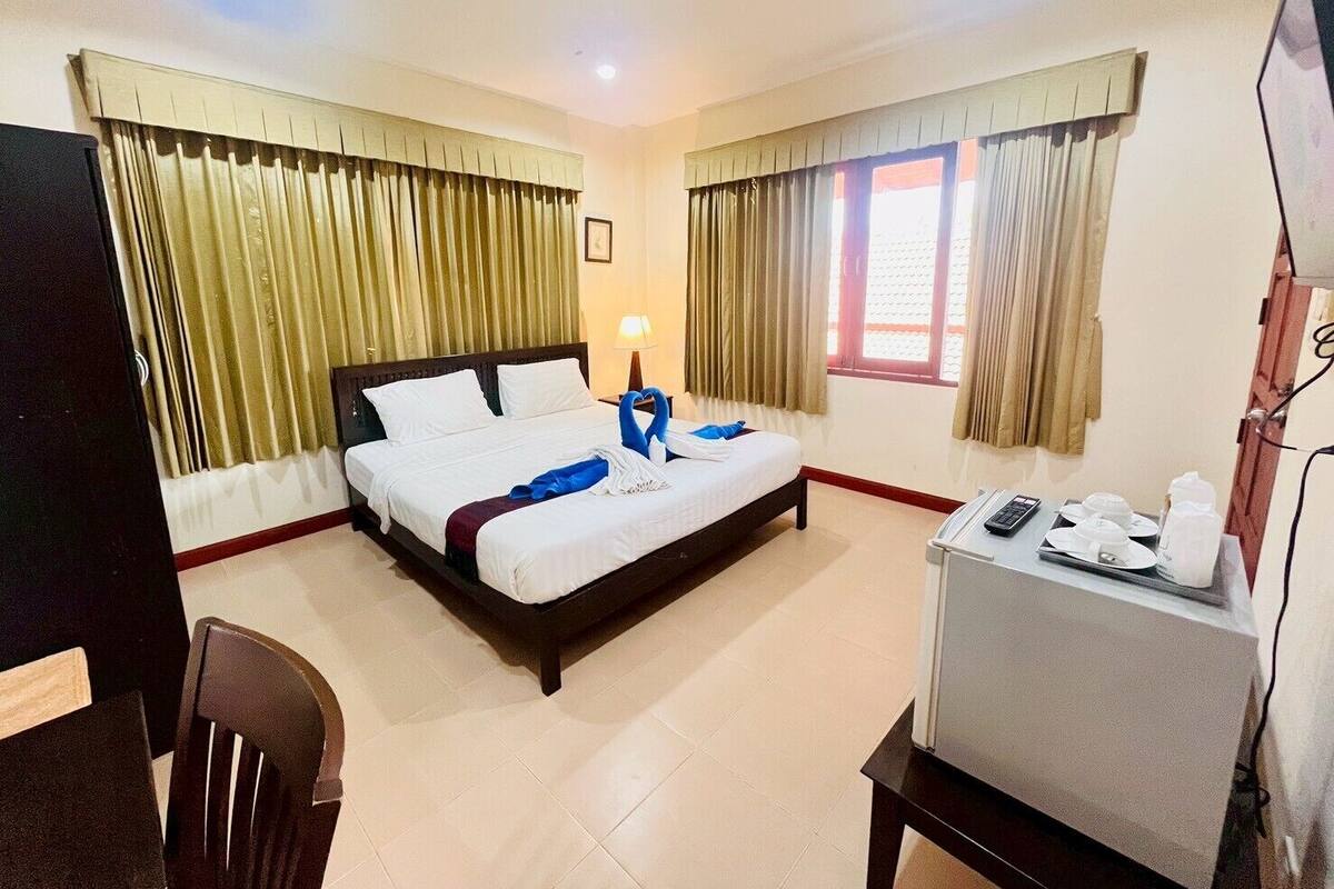 A hotel room with a bed, a desk with a phone and a lamp, curtains, and a window.