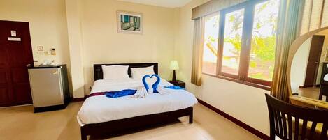 A hotel room with a bed, a desk, a chair, a small fridge, and a window with curtains.