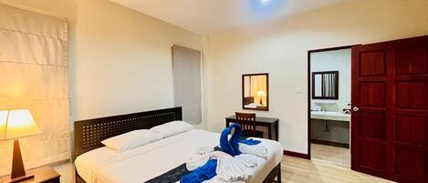 A hotel room with a bed, a nightstand, a lamp, a chair, a desk, a mirror, and a red door.