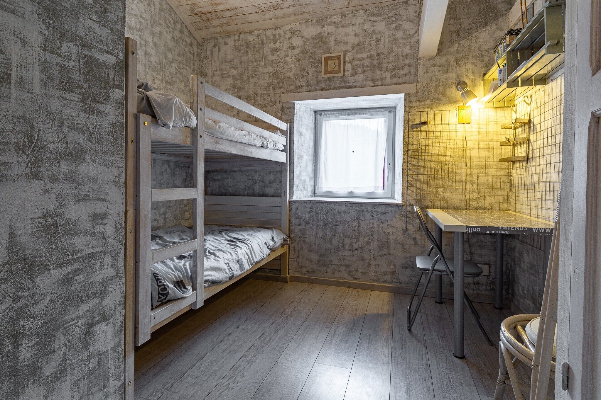 Une pièce de taille modeste, avec des lits superposés, une petite fenêtre, un coin cuisine et un plancher en bois.