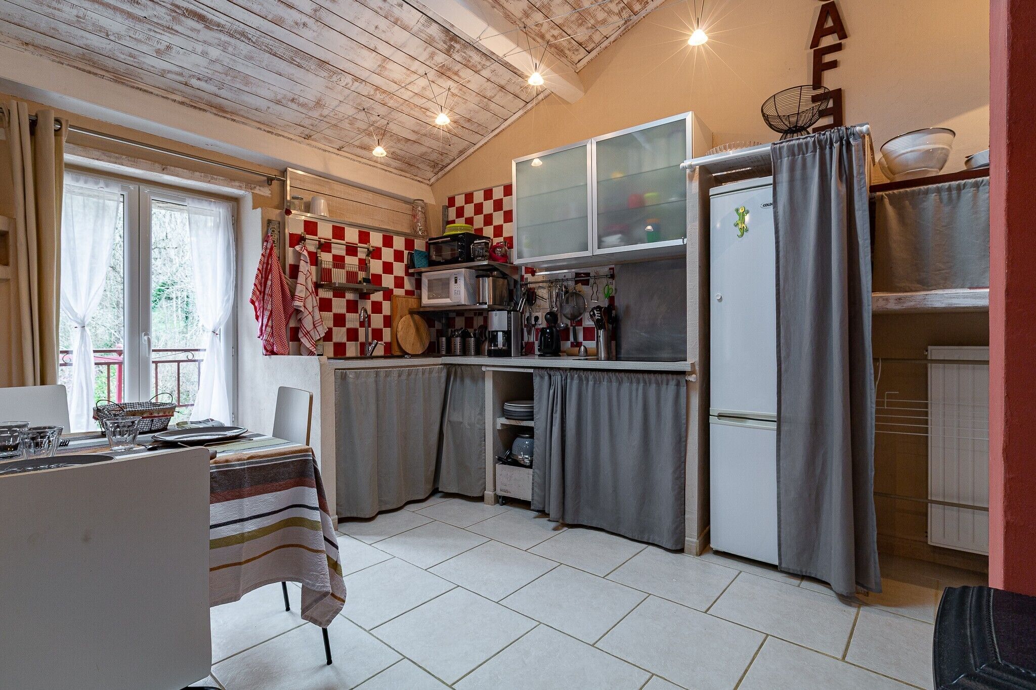 Una cocina compacta con una pared de cuadros, un refrigerador y una mesa de comedor con mantel a rayas.
