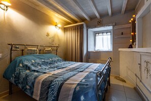 Un dormitorio con cama, lámparas de noche, una ventana con cortinas y un pequeño estante.
