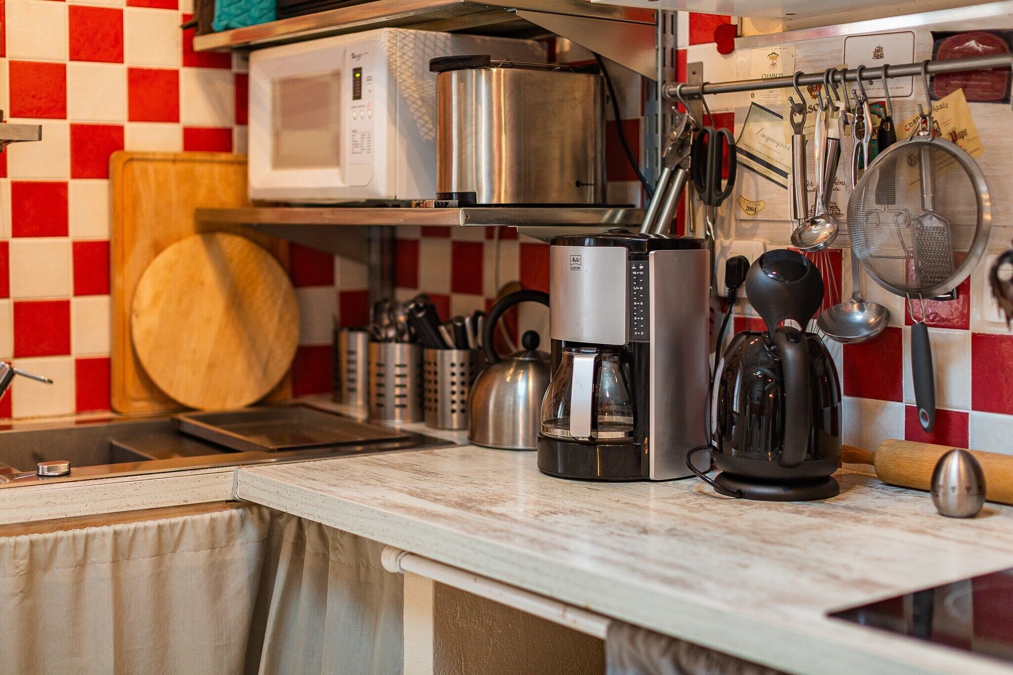 A kitchen with a microwave, coffee maker, kettle, and various utensils on the counter.