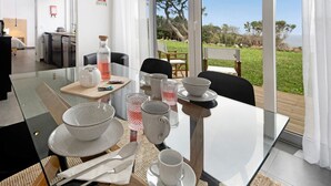 A dining area with a glass table, white plates, bowls, and cutlery. - Holiday Home "Rocha do Mar 1" with Sea View, Shared Pool & Wi-Fi (Biscoitos)