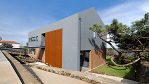 A modern building with a grey facade, wooden panel accents, and a stone pathway leading to the entrance. - Holiday Home "Rocha do Mar 1" with Sea View, Shared Pool & Wi-Fi (Biscoitos)