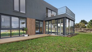 A modern two-story house with large windows, a balcony, and a well-maintained lawn. - Holiday Home "Rocha do Mar 1" with Sea View, Shared Pool & Wi-Fi (Biscoitos)