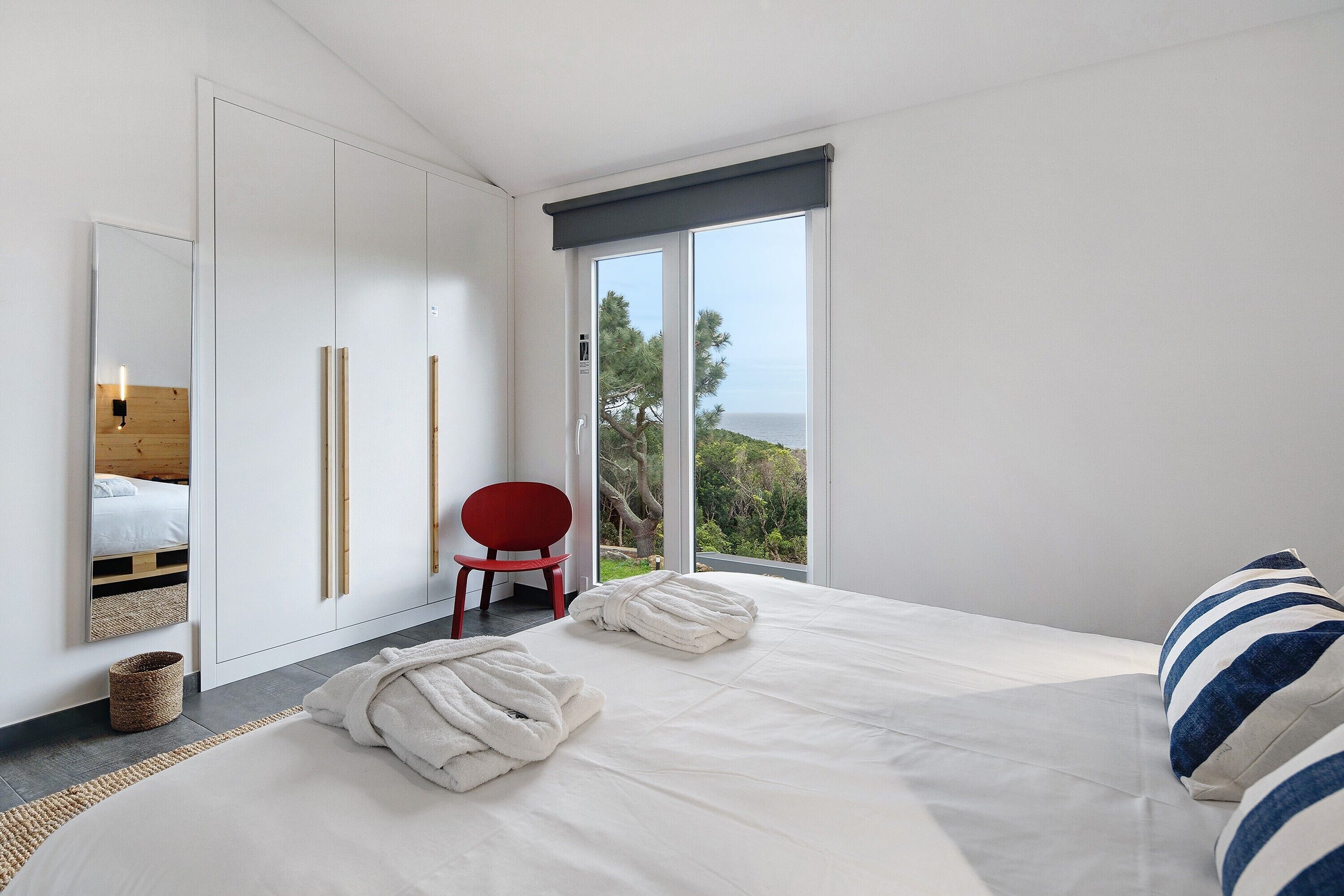 Ein Schlafzimmer mit einem Bett, einem roten Sessel, einem großen Fenster mit Blick und einem Kleiderschrank.