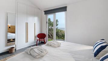 Ein Schlafzimmer mit einem Bett, einem roten Sessel, einem großen Fenster mit Blick und einem Kleiderschrank.