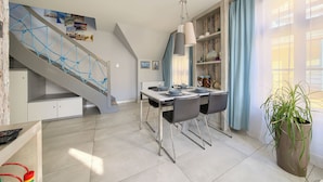 A modern kitchen with a dining area, a staircase with a rope net, and a potted plant.