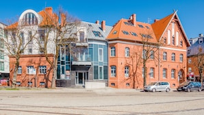 A row of buildings with a mix of modern and traditional architecture, including a prominent red brick building with a sloped roof and a glass-fronted structure with a curved roof.