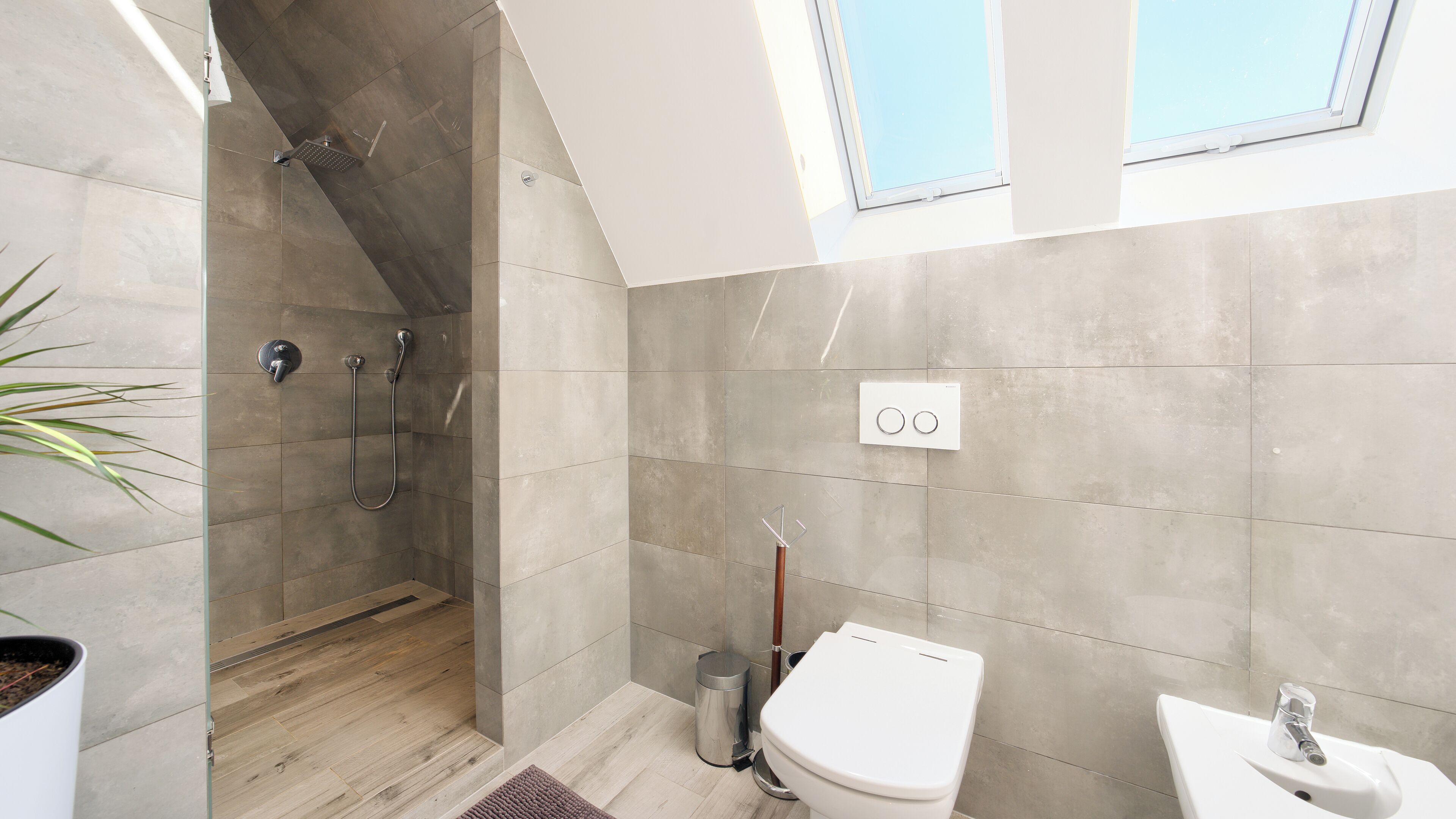 Un baño moderno con ducha, inodoro y lavabo, que cuenta con un tragaluz y una planta en maceta.
