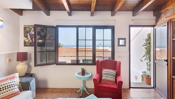 A room with a wooden ceiling, a red chair, a small table with a plant, a window with a view, and a door leading outside. - Holiday Home 'Villa Floti With Sea View' with Sea Views, Wi-Fi and Air Conditioning (Telde)
