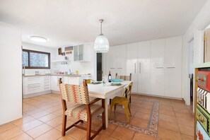 A kitchen with white cabinets, a dining table with chairs, a hanging light fixture, and a patterned rug.