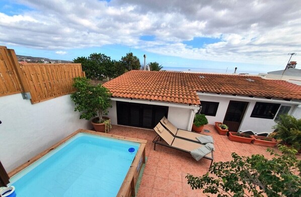 Propiedad residencial con piscina, sillas de descanso, plantas en macetas y tejado de baldosas.
