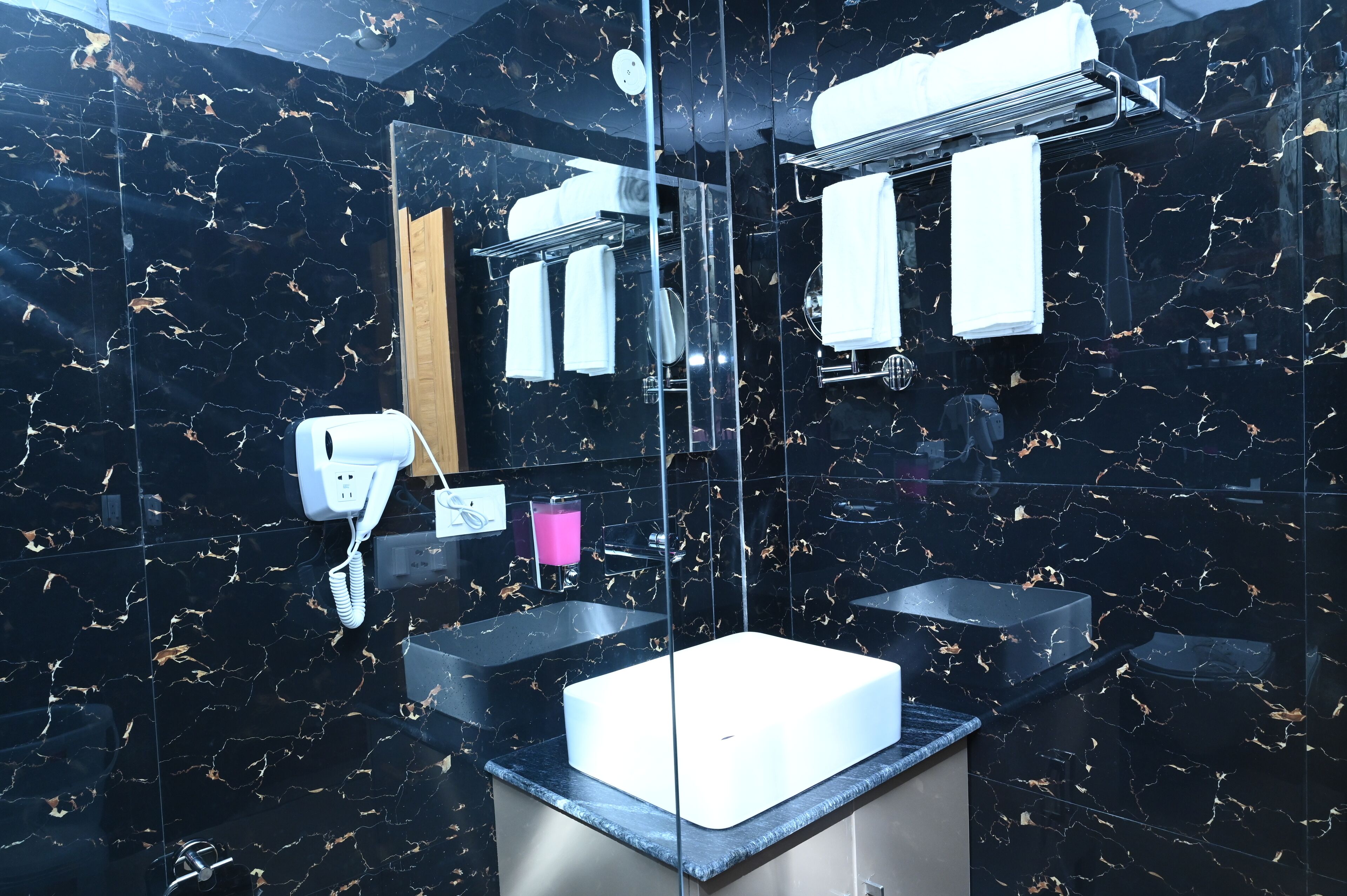 A modern bathroom with black marble walls, a white sink, and a glass partition.