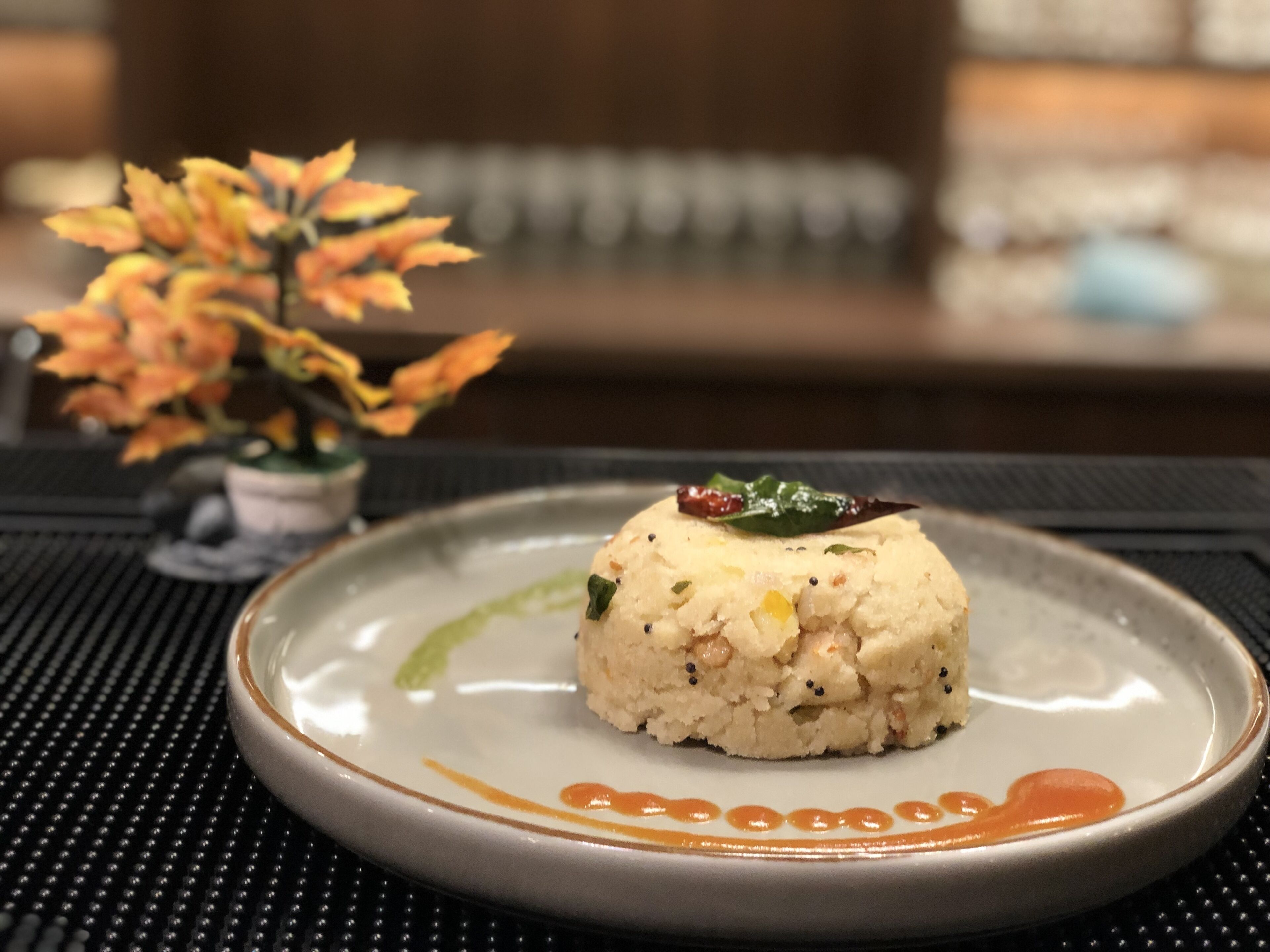Un plato con una porción de arroz y una hoja verde encima, sobre un mantel con textura.